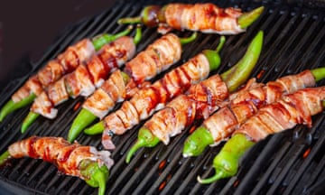 Jalapeno peppers on burning, grill. Spicy peppers stuffed with cream cheese and wrapped in bacon. Top view with selective focus.