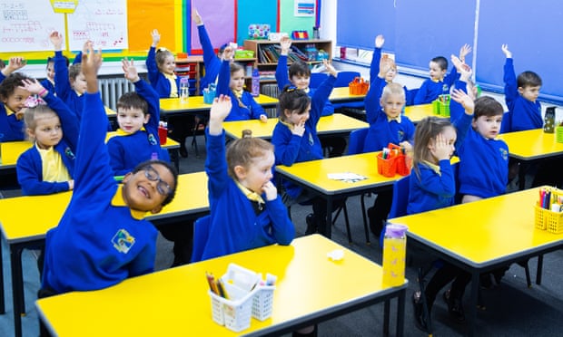 Children sitting at tables with their hands raised
