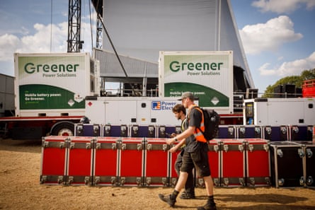 Two men walk past equipment being set up for the stage