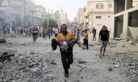 A Palestinian man carries a wounded girl at the site of Israeli strikes, in Khan Younis in the southern Gaza Strip, 14 October.