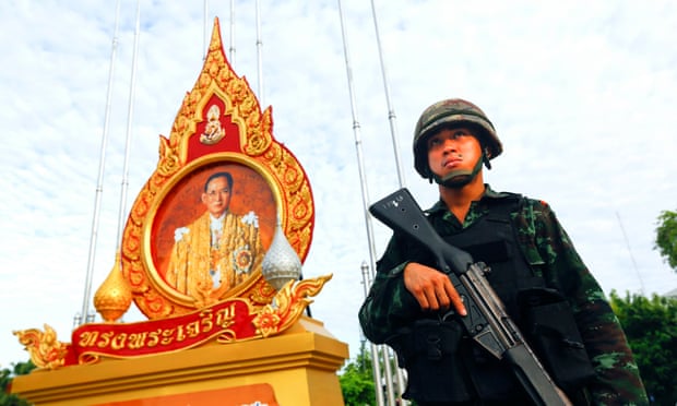 A soldier stands guard beneath a portrait of King Bhumibol Adulyadej outside Government House in Bangkok, Thailand.