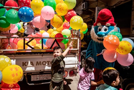 A mascot dressed as a Smurf hands balloons to children as part of a local NGO awareness campaign to encourage hand-washing, hygiene, and social distancing in response to the pandemic in Qamishli, Syria.