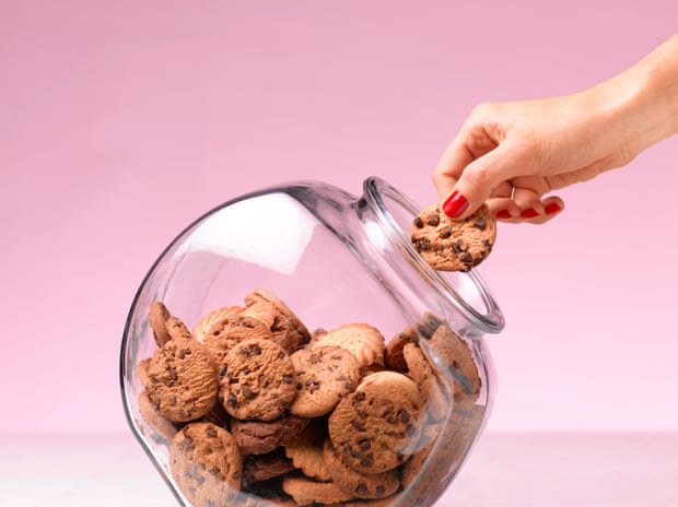 A woman's hand with red painted fingernails takes a cookie out of a jar