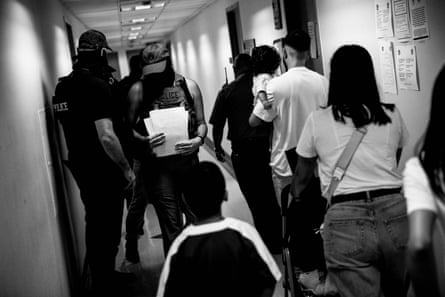 A man holding a baby, a woman pushing a stroller, a young girl and a young boy walk past masked agents
