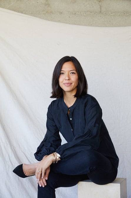 A woman in a navy blue blouse and trousers sitting on a riser, in front of a white fabric backdrop