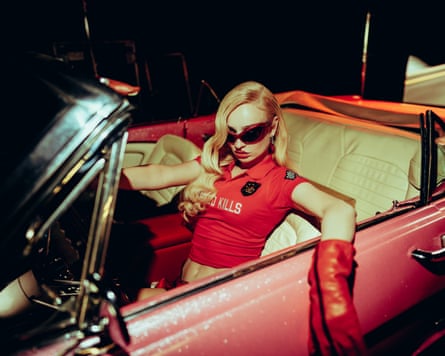 Kim Petras in red top and high red gloves and shades in a red sports car looking sultry