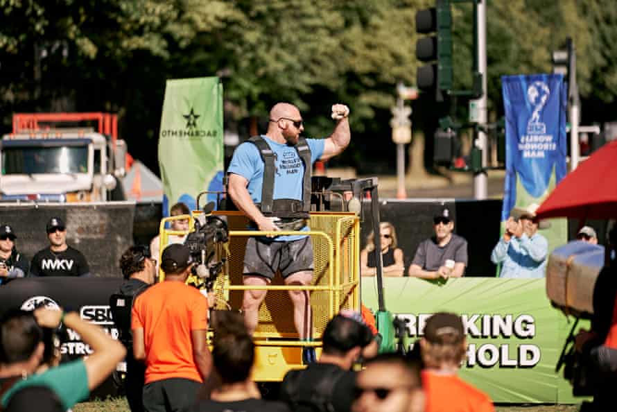 another bald, bearded man curls his arm while crowd looks