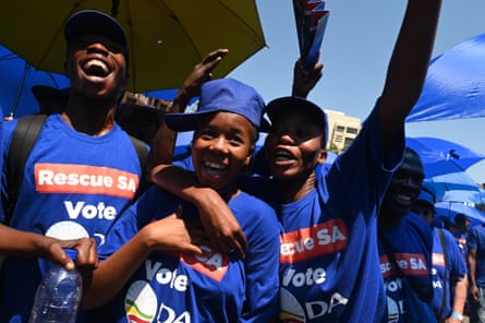 Three young black Africans in blue T-shirts, with the slogan “Rescue SA – vote DA”, smile and laugh at something off-camera