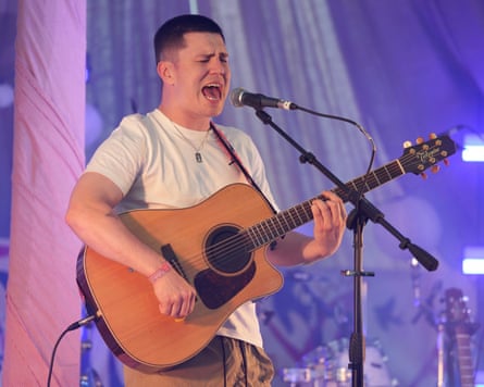 Rowe, holding a guitar, sings into a microphone on stage