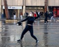Dressed in black and wearing a white mask, a protester throws a cobblestone during an anti-government demonstration in the streets of Tirana, with other protesters nearby