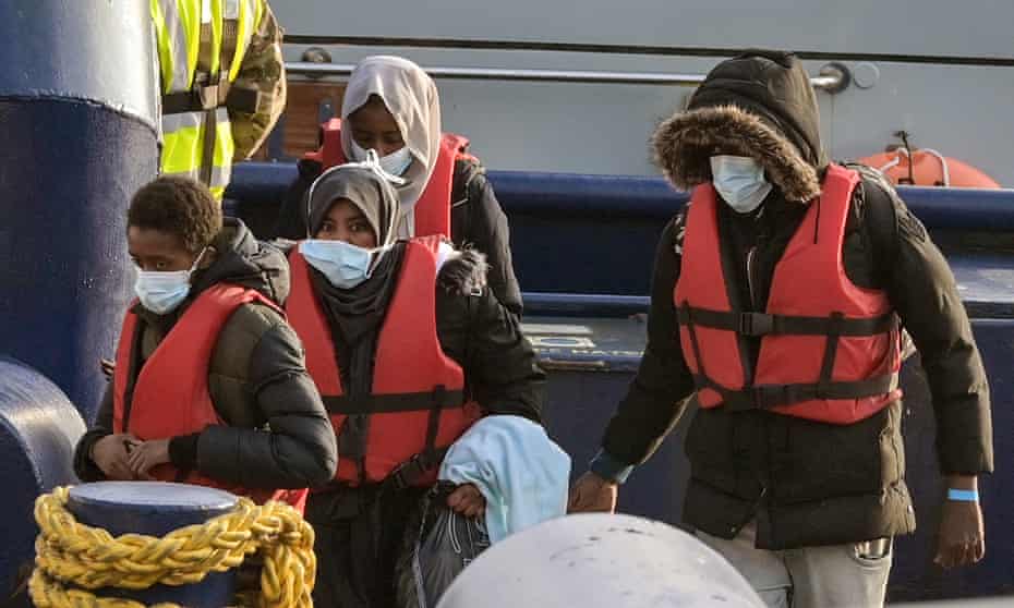 Refugees (men and women) wear life jackets and face masks