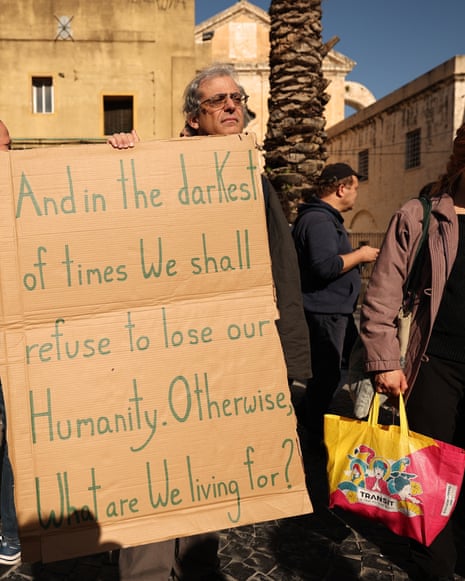A man holds a sign saying: 'And in the darkest of times we shall refuse to lose our humanity. Otherwise, what are we living for?'