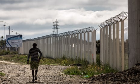 A migrant walks along a perimeter fence in Calais, France