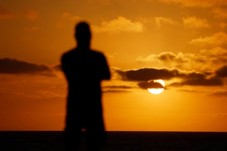 silhouette of a person looking at the sunset by water