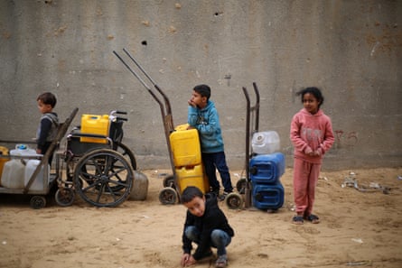 Small children queue for water with plastic canisters on trolleys