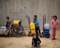 Children with yellow water canisters on trolleys and a wheelchair at a refugee camp