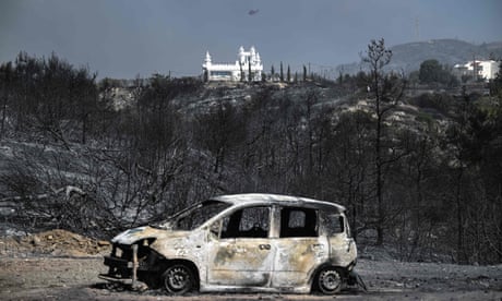 A burned-out car against a background of charred trees and hills