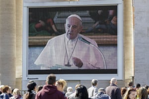 Faithful watch Pope Francis deliver the Angelus prayer on a giant screen, in St. Peter’s Square, at the Vatican