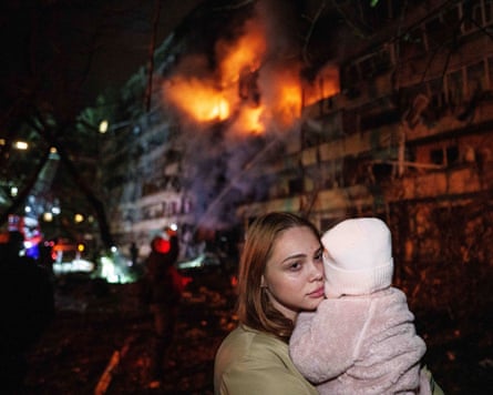 A woman holds her daughter in front of a residential building on fire