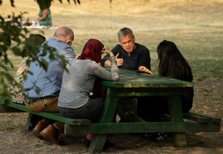 Duncan Ali and Neha Gohil sit at a picnic bench with three other people in a park.