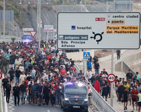 Police officers and Spanish soldiers escorted a large group of people on foot along a road