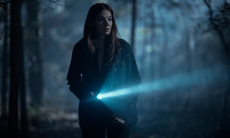 A series still showing a woman walking in the forest with a flashlight