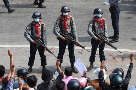 Three soldiers with rifles and helmets face a crowd of young people waving in the air