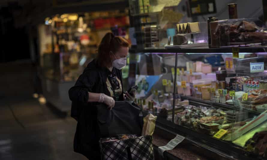 A woman wearing a mask to prevent the spread of the coronavirus purchases food in a market in Madrid, Spain.