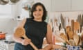 Samin Nosrat, with curly shoulder-length hair and in a sleeveless dress, grins as she leans on a kitchen counter holding a long wooden spoon