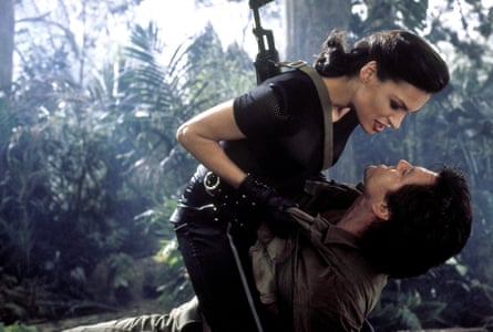 She straddles Pierce Brosnan (outdoors & fully clothed), crushing him between her thighs