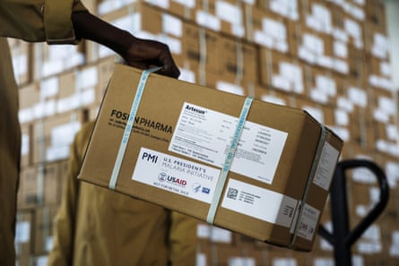 A box of Artesunate malaria medication is transported. Many more similar boxes can be seen behind it