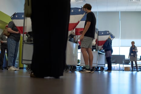 A young man votes at a flag-draped booth during early voting, with others voting nearby