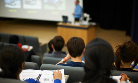 Students sit in a lecture theatre with a person teaching at the front.