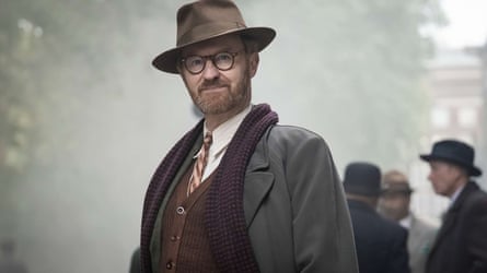 A man looks at the camera, wearing post-second world war smart clothing including scarf and wide-brimmed hat