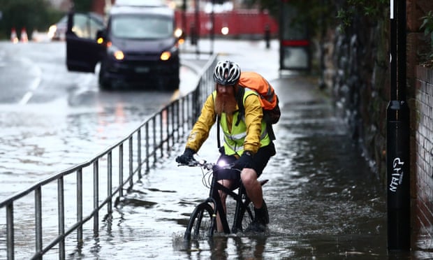 Man cycling along pavement through water up to his hubs