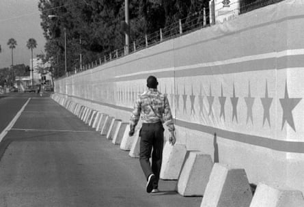A person walking on a sidewalk alongside a high wall.