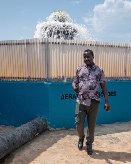 A man stands in front of what looks like a fountain in a fenced-off water facility