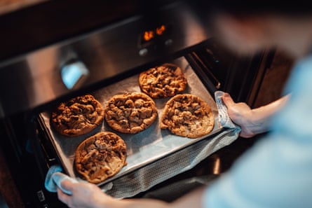 Over the shoulder view of young woman taking out freshly baked cookies from the oven