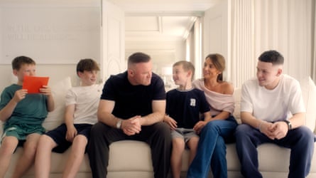 Wayne and Coleen on a sofa in a still from the show The Real Rooneys, with their sons (from left) Kit, Klay, Cass and Kai