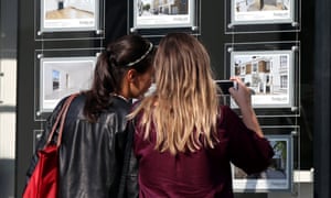 two young women looking at houses for sale in an estate agent's window.