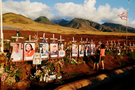 Two people in front of a row of photos with crosses behind them