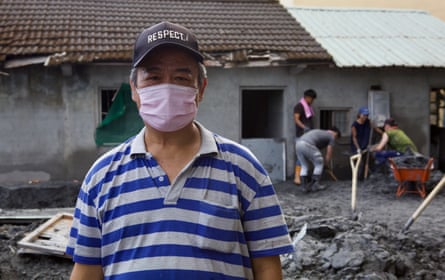 Peng Shin-yi stands outside his destroyed house, while volunteers behind help to dig out tonnes of mud.