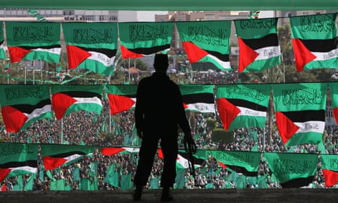 A large crowd with Palestinian flags and in the foreground the silhouette of a security guard at a rally marking the 21st anniversary of Hamas’s creation in Gaza City in 2008.