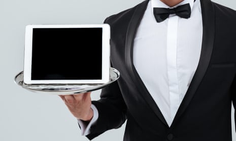 A butler in tuxedo with bowtie holding blank screen tablet on tray.