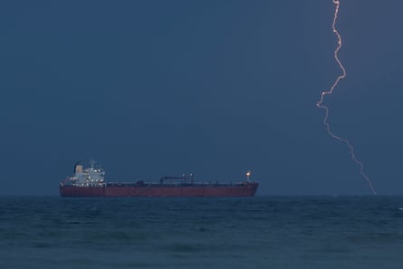 A red oil tanker with a flash of lightning behind it