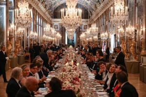 Guests seen sitting down to eat inside the Palace of Versailles, with numerous glittering chandeliers above