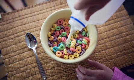 A young girl pours milk into a bowl of colorful breakfast cereal