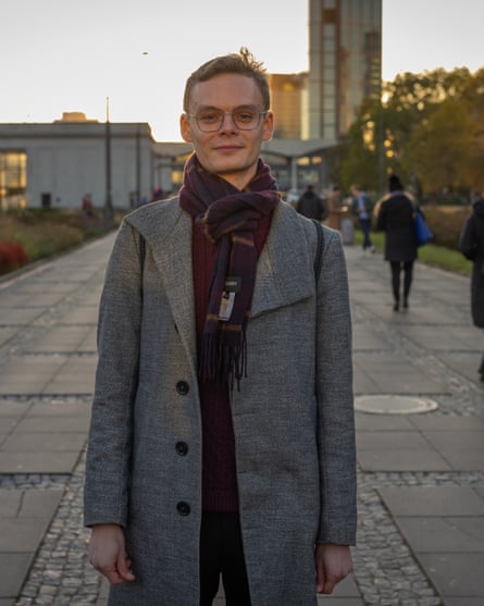 Man wearing grey coat and a scarf looks towards the camera