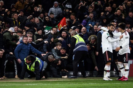 Bruno Fernandes of Manchester United celebrates with teammates after scoring the team’s third goal as fans knock over the advertising boards during the Carabao Cup Semi Final 1st Leg match between Nottingham Forest and Manchester United.