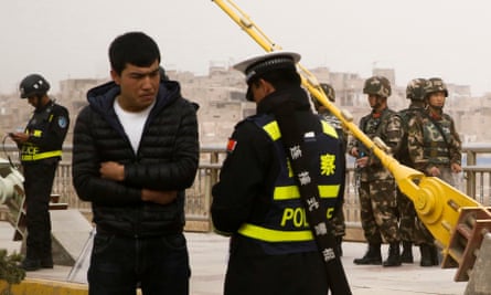 A police officer checks the identity card of a man as security forces keep watch in a street in Kashgar, Xinjiang